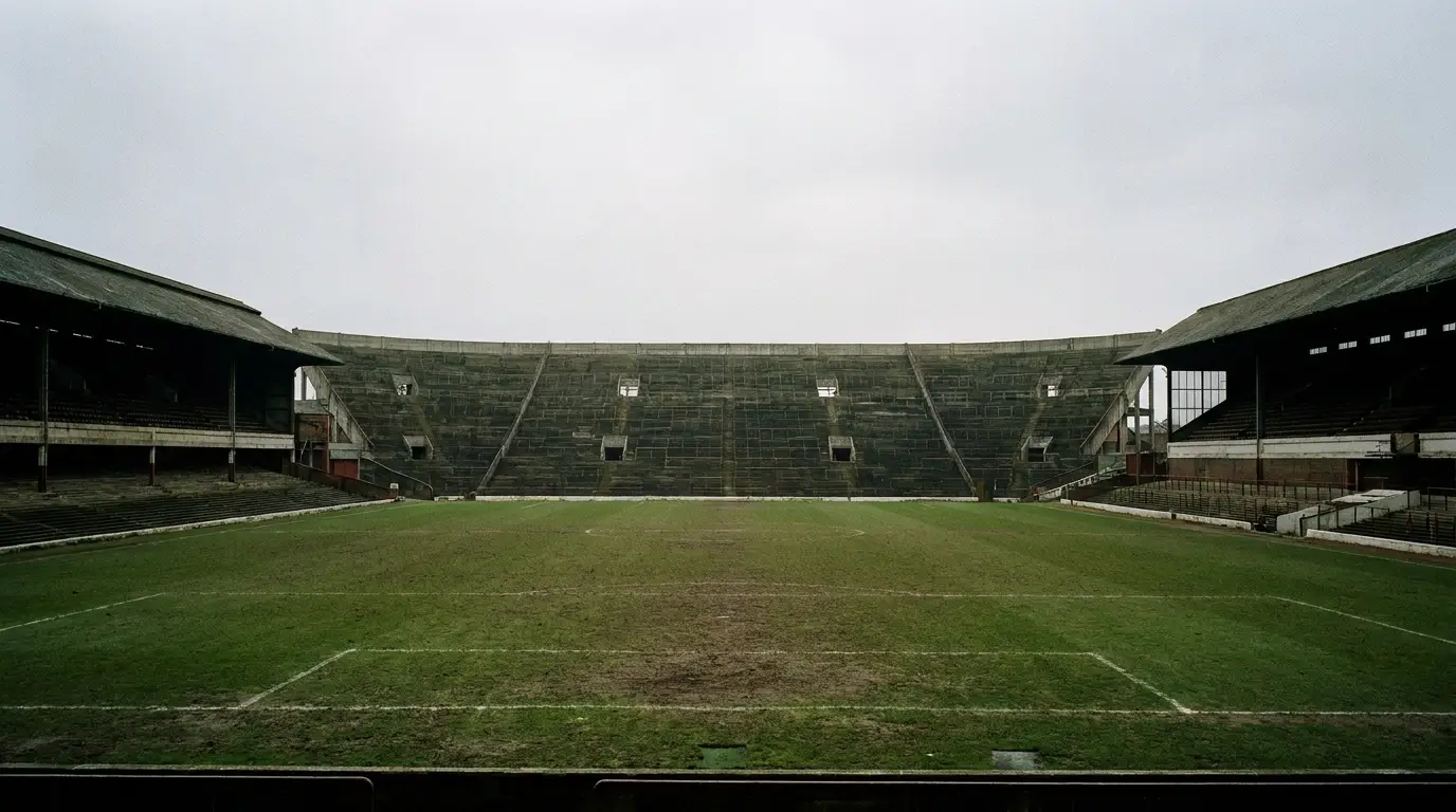 Empty soccer stadium with green field and aging bleachers under overcast sky