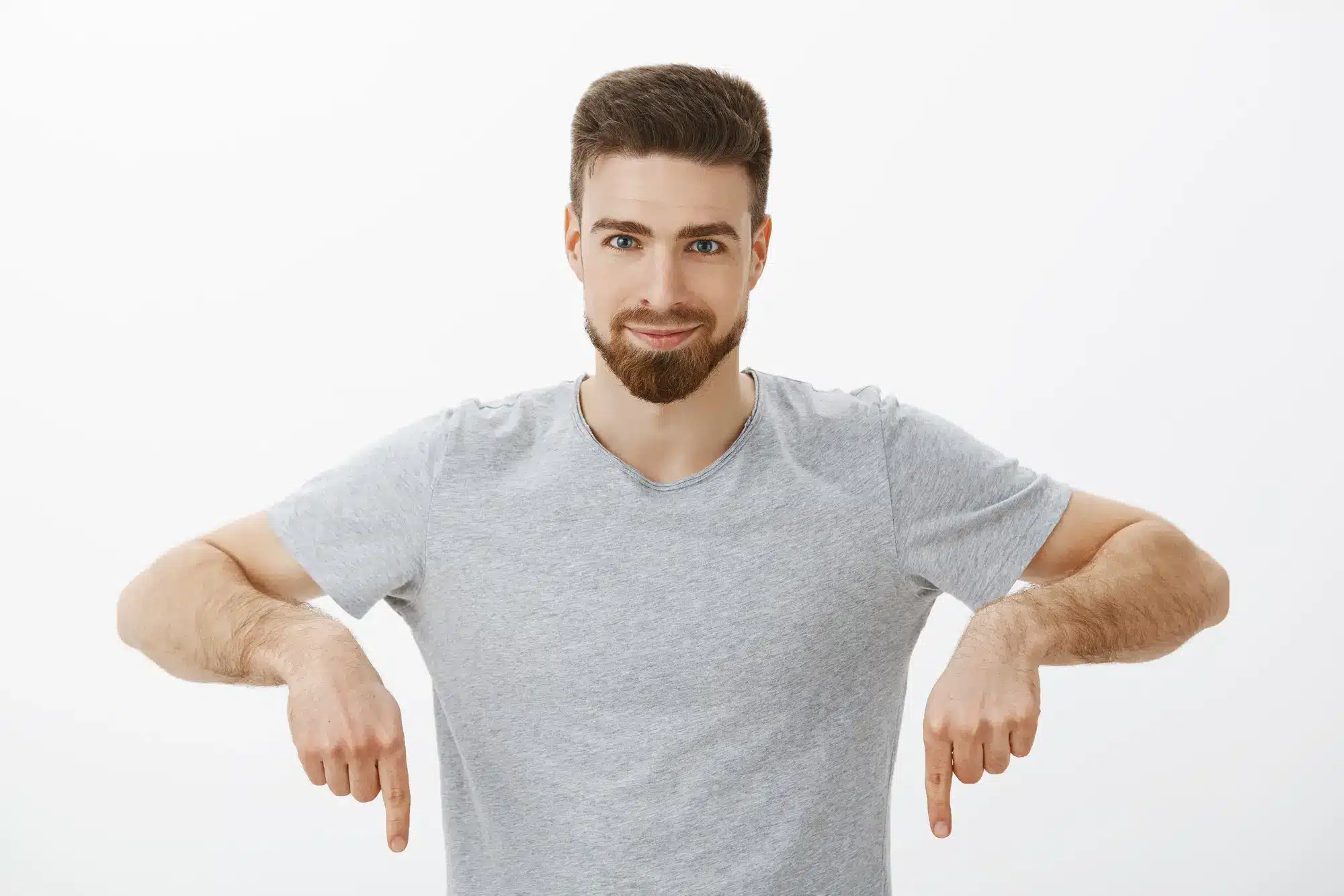 Man in gray t-shirt gesturing downward with both hands against white background