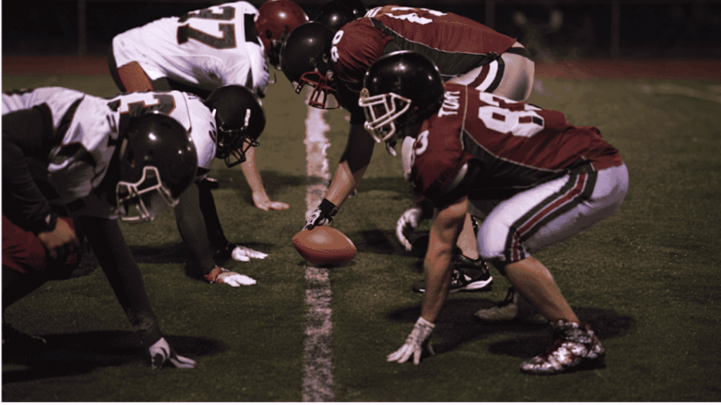 football players line up at the line of scrimmage preparing for the snap during a nighttime game on the field (2)