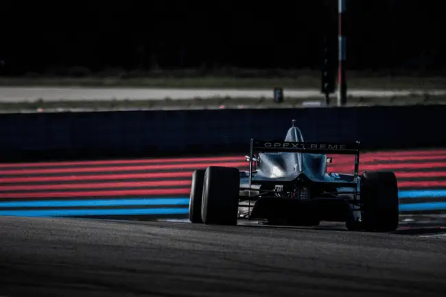 Race car on track with red and blue painted lines under cloudy sky