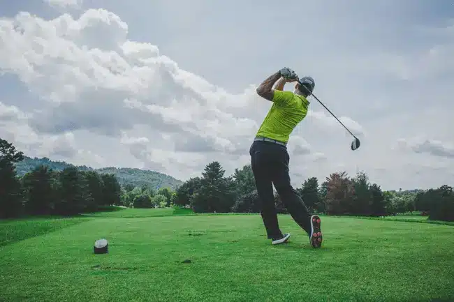 Golfer in bright attire swinging on lush green course under cloudy sky