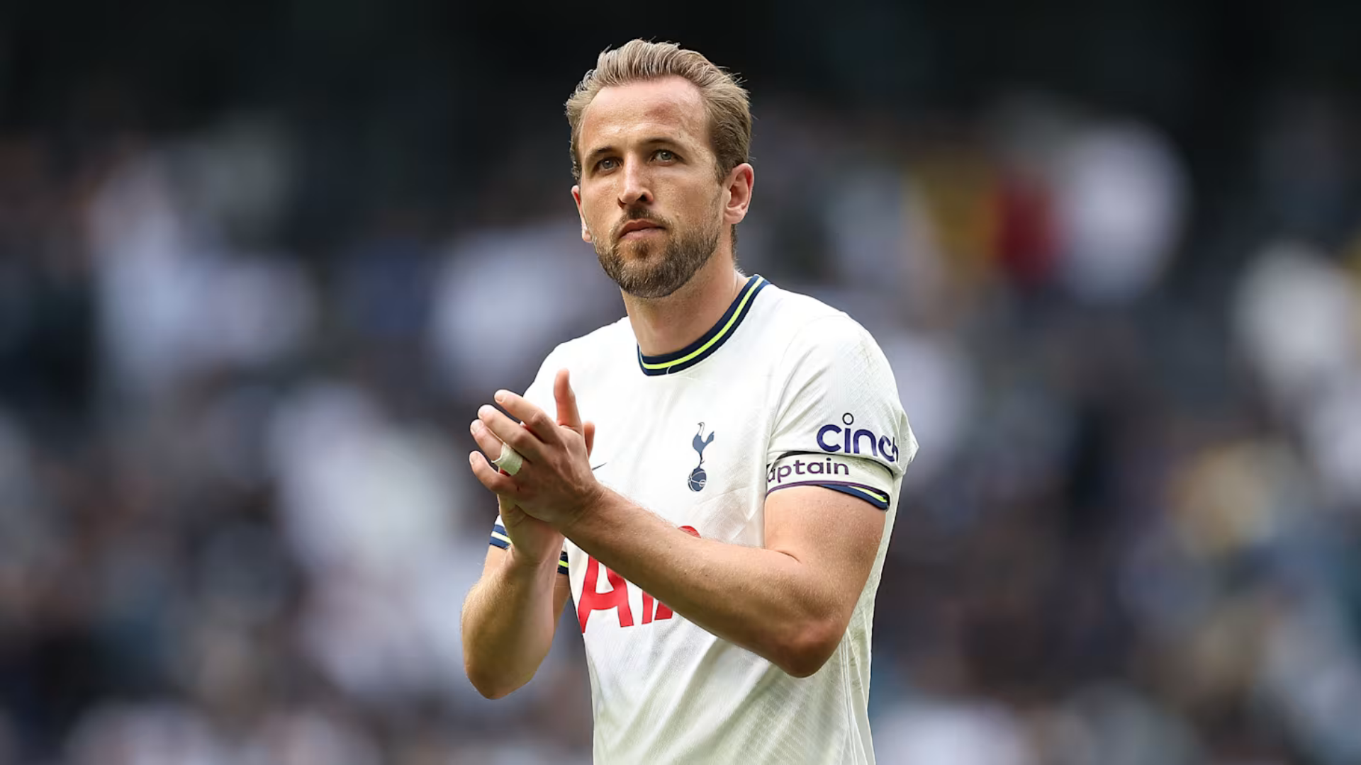 harry kane wearing a white club jersey clapping hands on the field during a stadium match