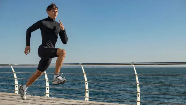 Man running along a boardwalk by the ocean under clear blue sky