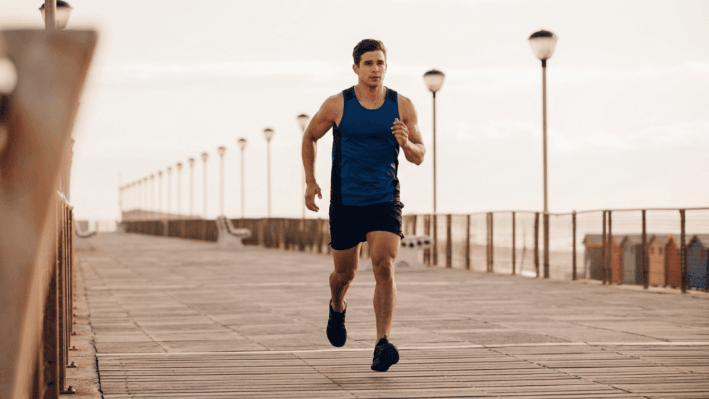 man jogging on a seaside boardwalk at sunrise in blue athletic wear