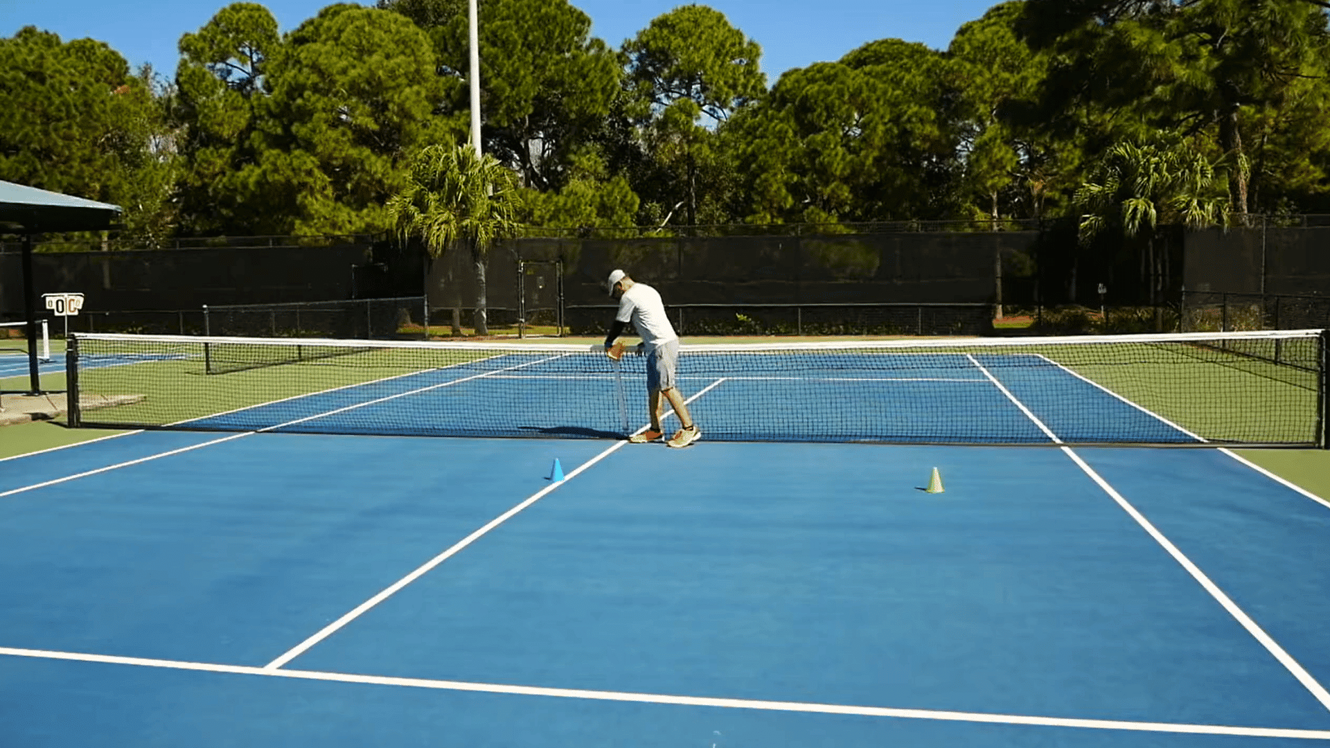 Man adjusting a tennis net while cones mark temporary pickleball boundaries on the court