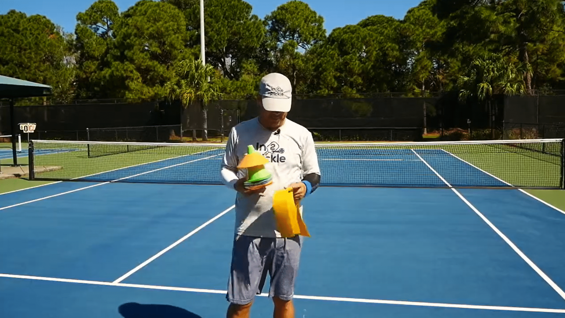 Man holding colorful court markers while setting up a temporary pickleball court on a tennis court