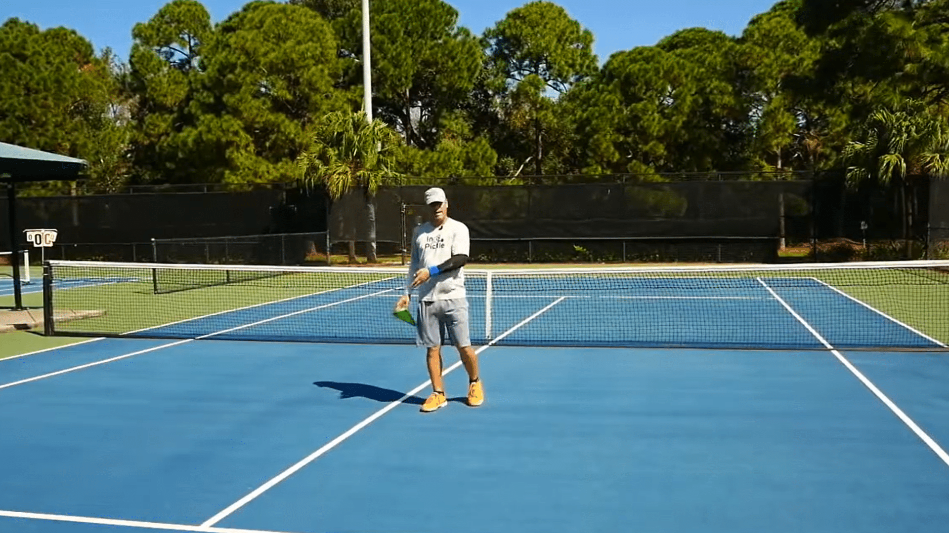 Man pointing to temporary pickleball court markings on a tennis court during court setup demonstration