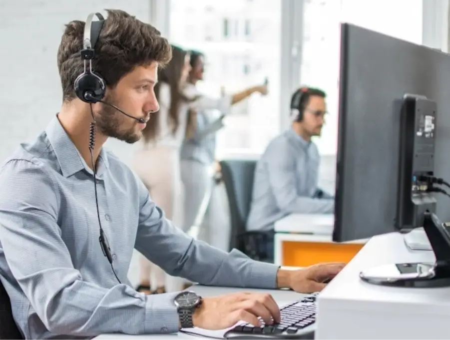 Man with a headset working at a computer in a bright office setting