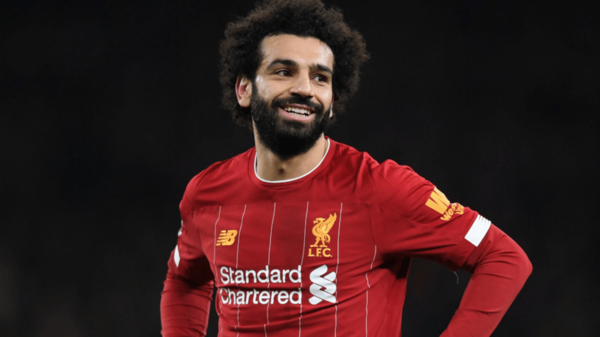 mohamed salah wearing a red club jersey smiling while standing on the field during a match