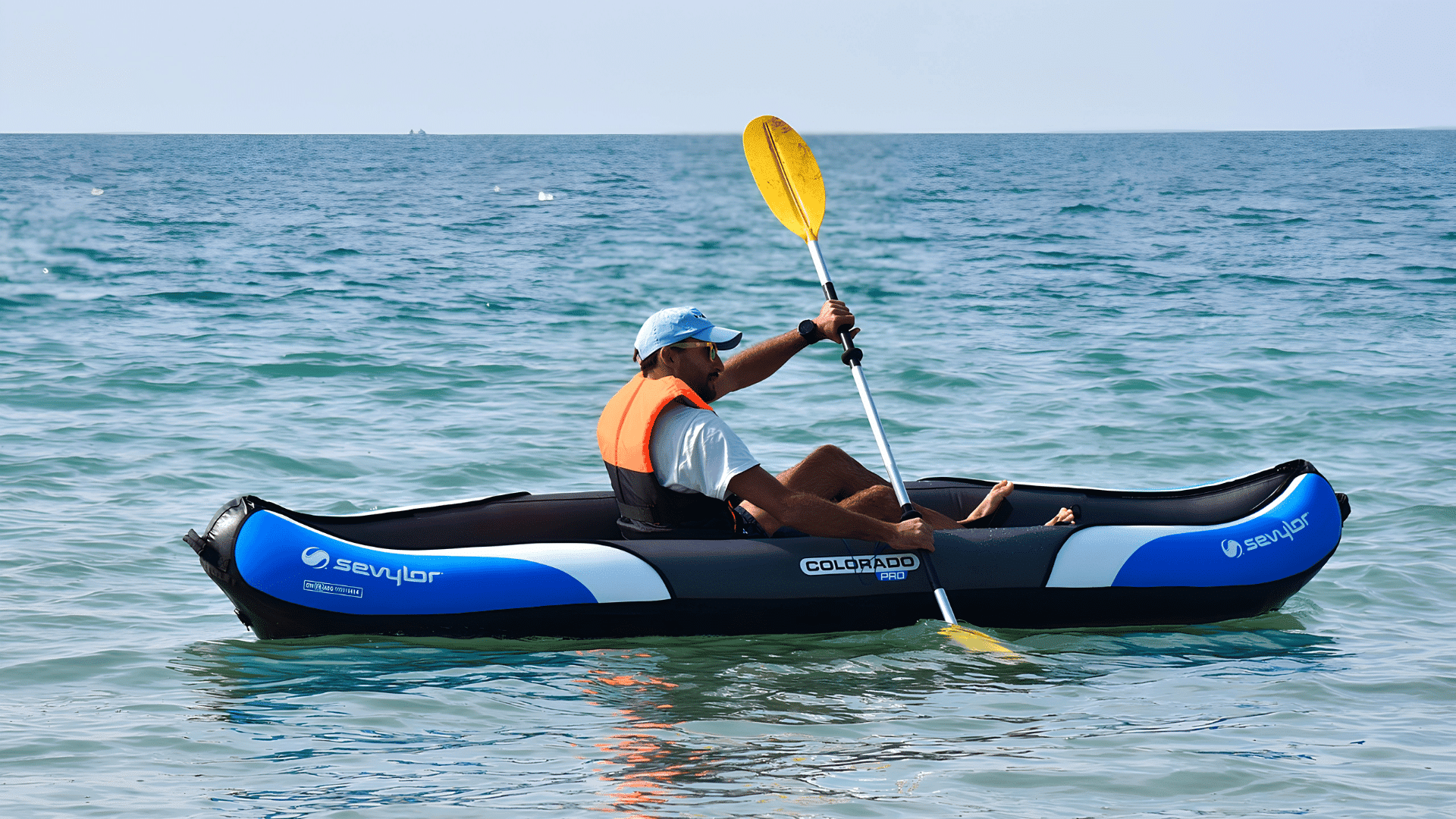 person paddling an inflatable kayak across calm sea water while wearing a life vest and holding a yellow paddle