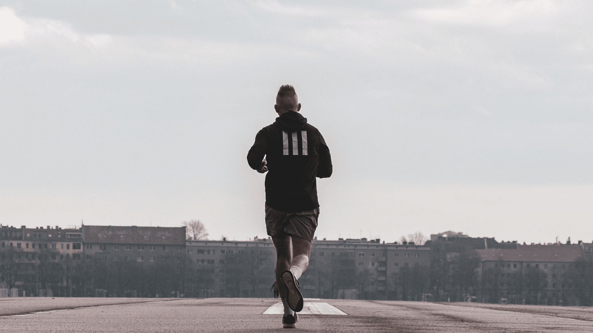 person running along a wide city road beneath cloudy skies with distant buildings visible in the background