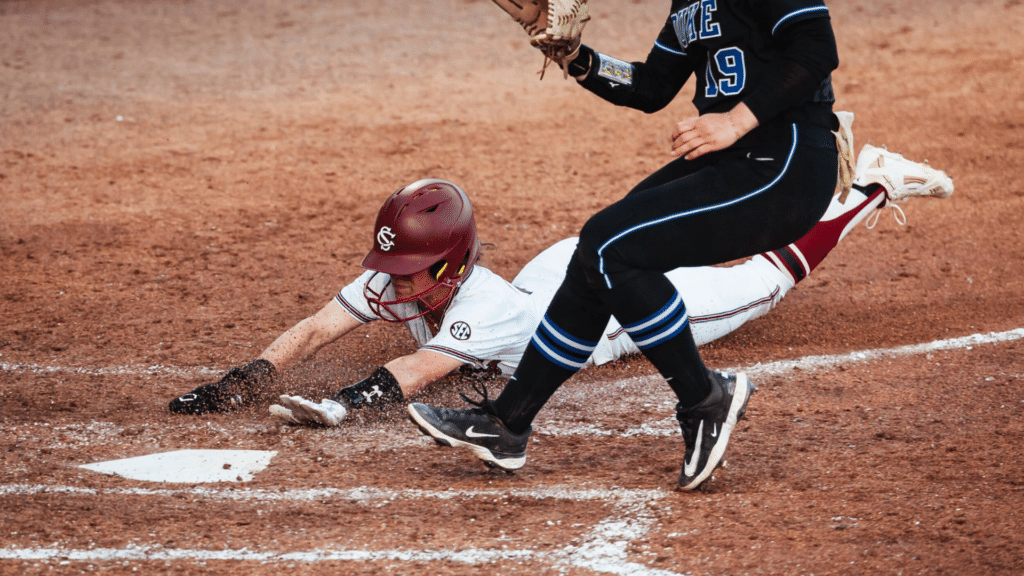 player dives headfirst toward home plate as opposing catcher reaches with a glove for a close play at the plate