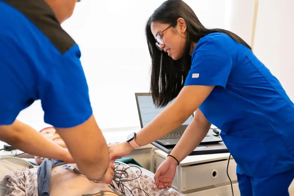 Medical students in blue scrubs performing CPR on mannequin in clinical training room