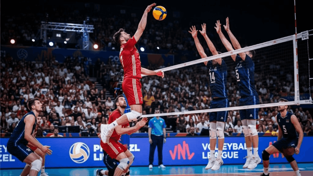 Professional volleyball player spikes the ball over a triple block during an indoor international match with teammates opponents and a packed crowd watching from the stands