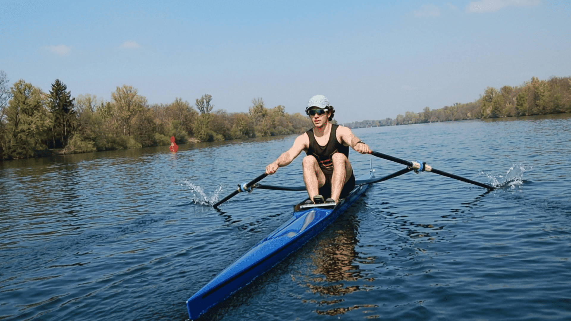 Single scull rower training on a calm lake with oars splashing in the water