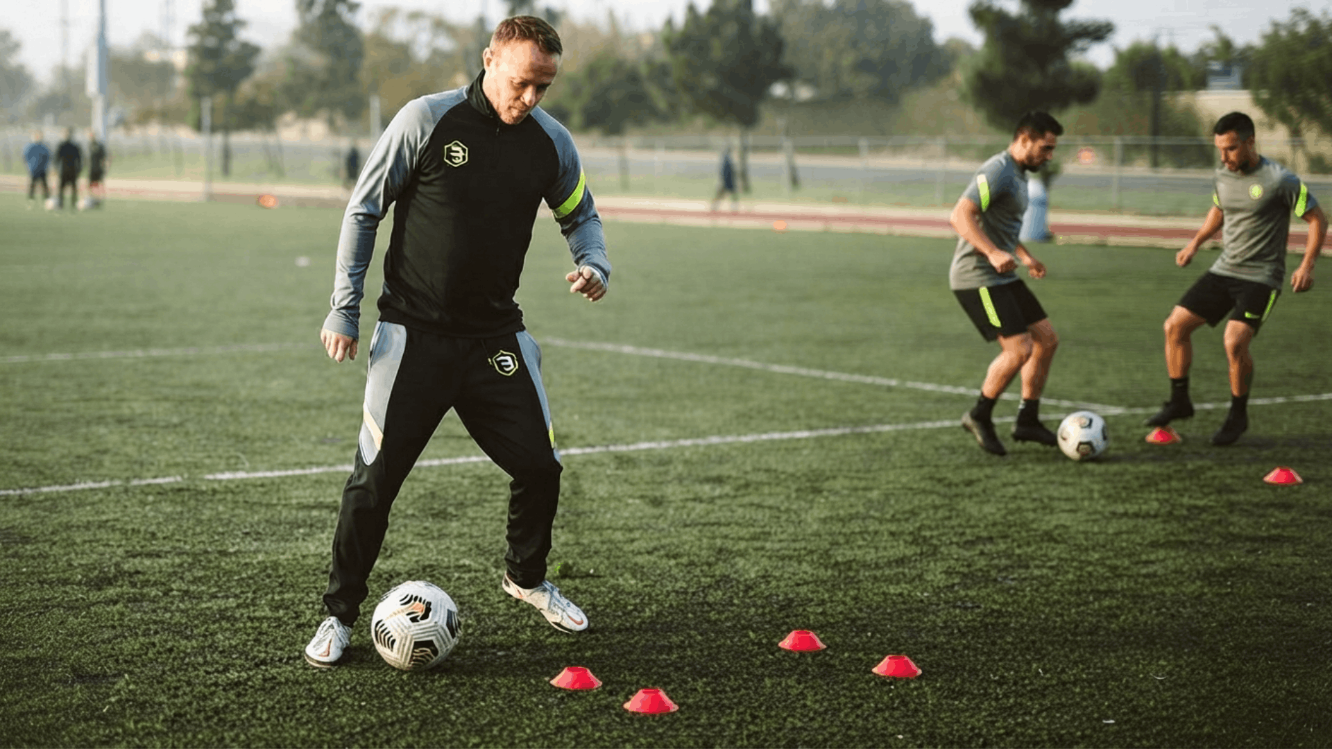 soccer coach demonstrating ball control drills with training cones while players practice skills on an outdoor field