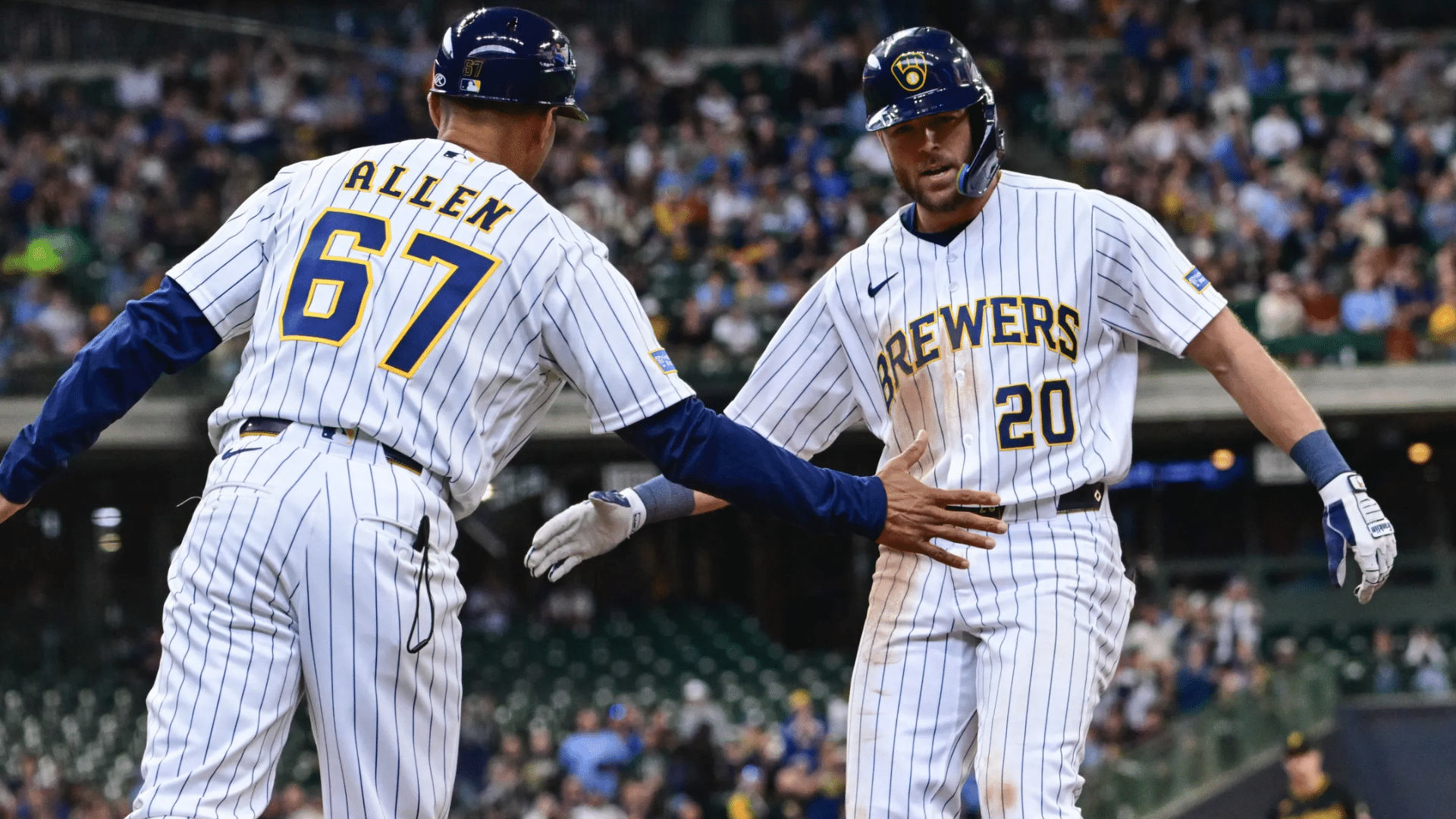 two baseball players in brewers uniforms exchange a celebratory hand slap on the field with a crowd in the stadium behind them (1)