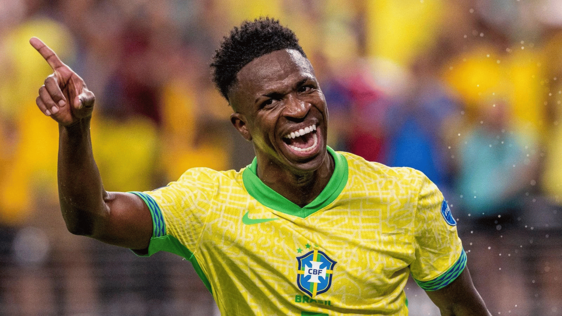 vinícius Júnior wearing a yellow national team jersey celebrating with a raised hand during a stadium match