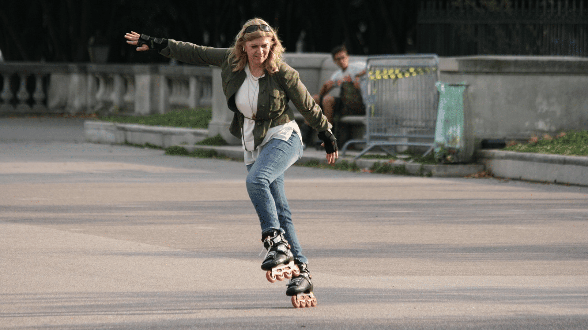 woman inline skating across a paved park path while balancing with outstretched arms and wearing protective wrist guards