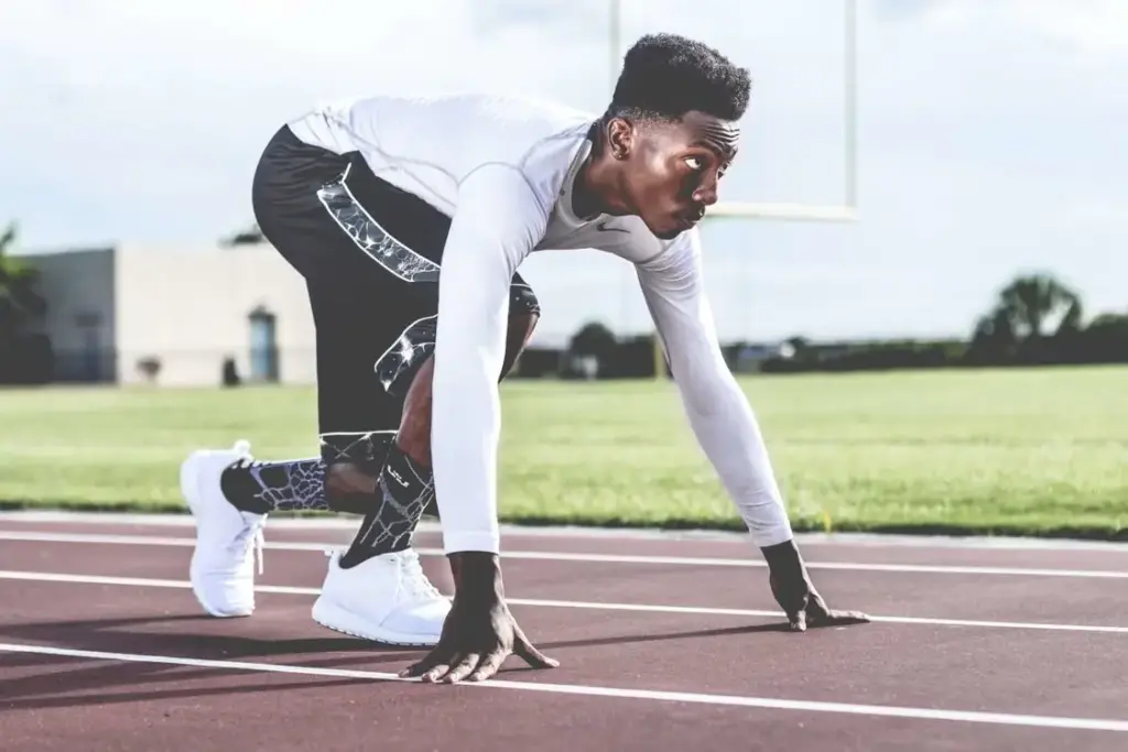 Athlete in starting position on outdoor track wearing athletic gear and white sneakers