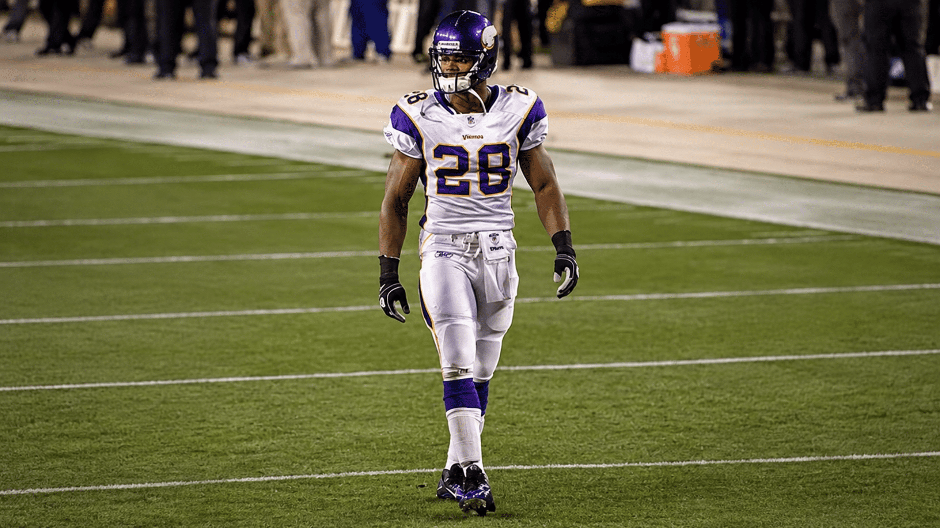 football player wearing number 28 in a white and purple uniform walking across the field during a game