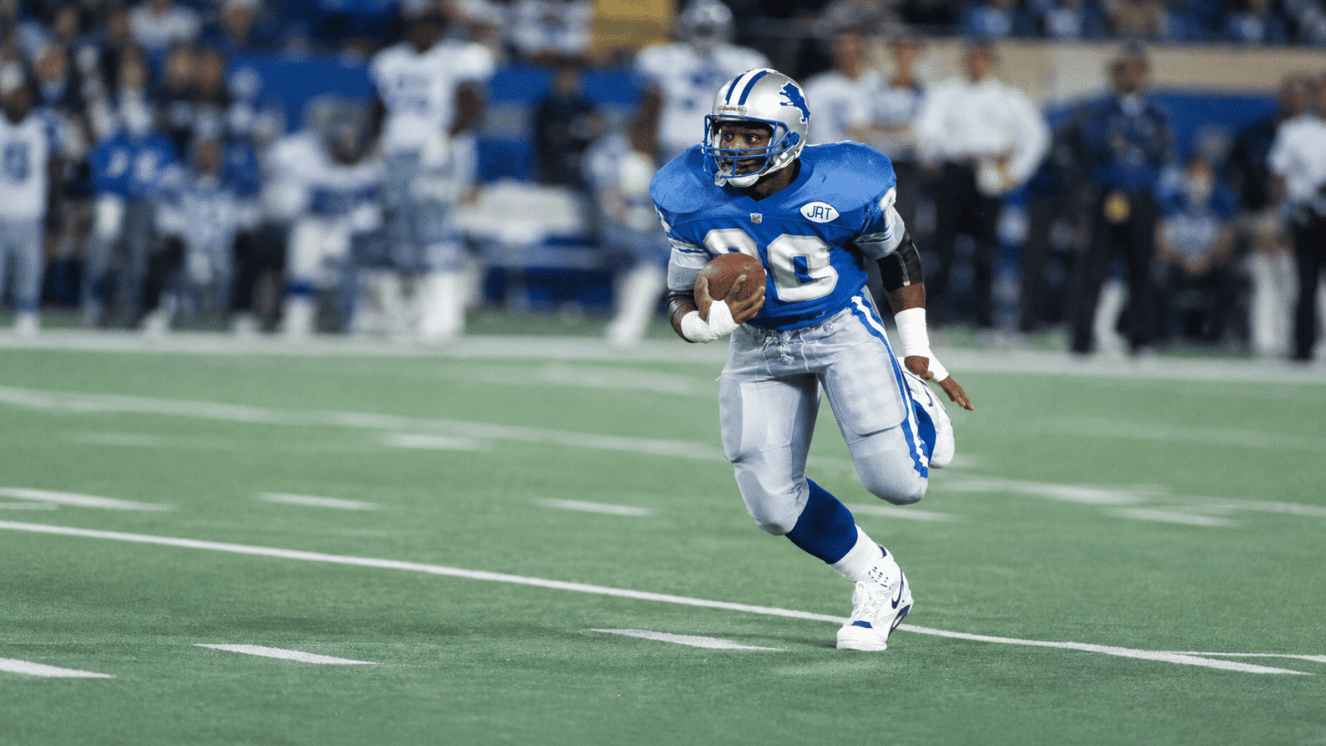football player in a blue and silver uniform running across the field while carrying the ball during a game