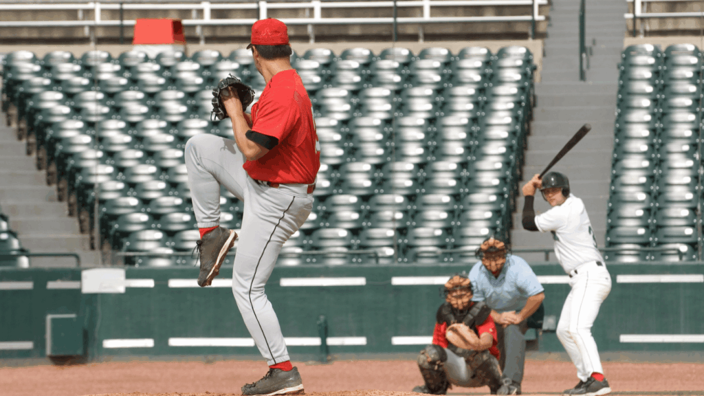 baseball pitcher in red uniform winding up on the mound as a batter waits at home plate