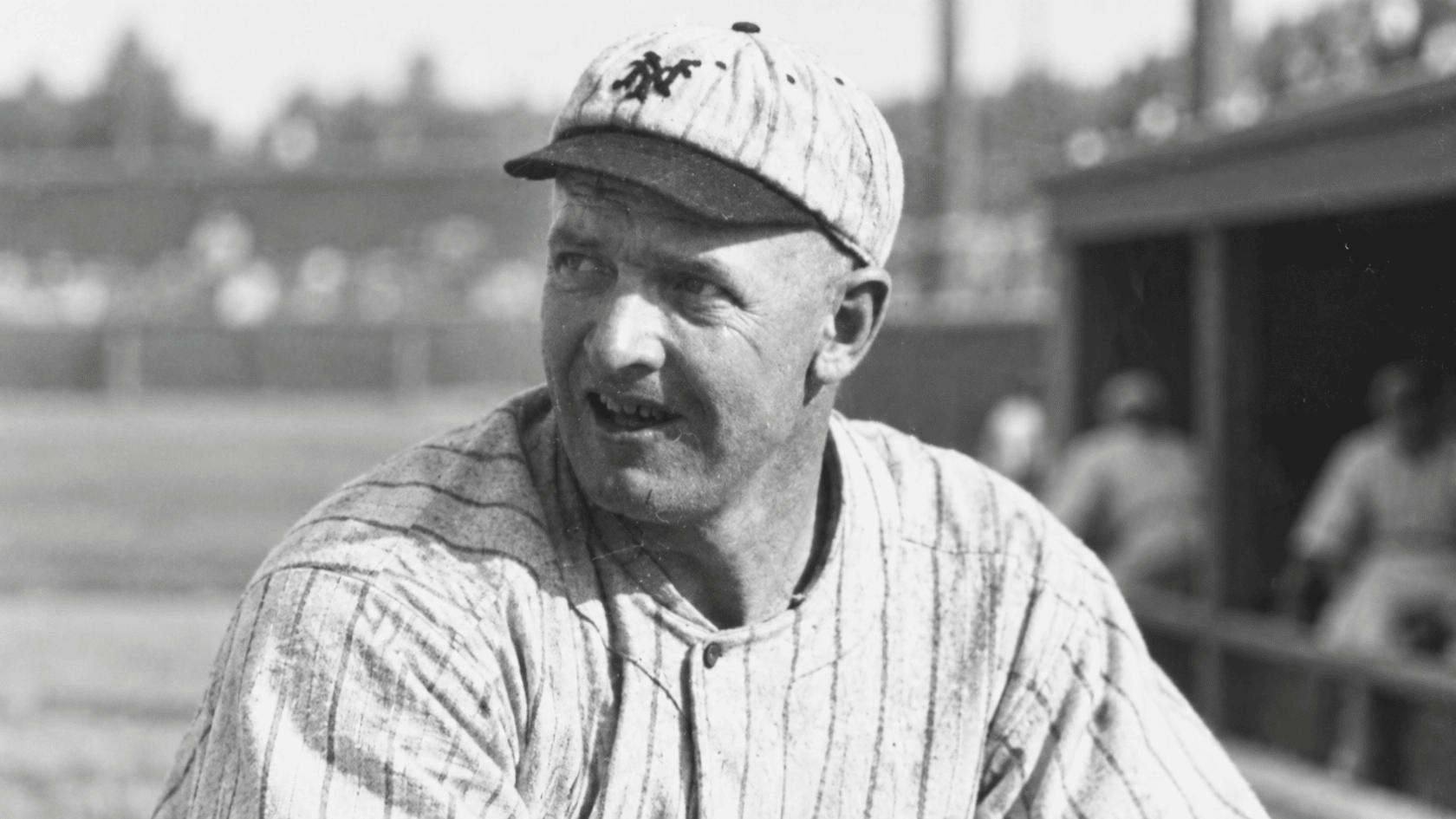 historic black and white image of a baseball pitcher wearing a striped uniform and baseball cap