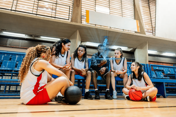 Basketball team in red and white uniforms listening to coach indoors on gym court
