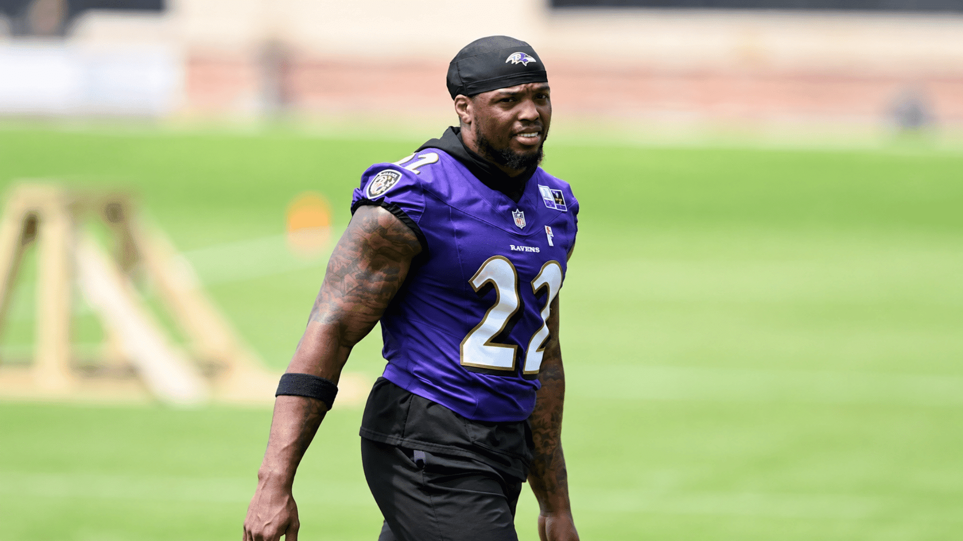 football player wearing a purple number 22 jersey walking across a sunny outdoor practice field