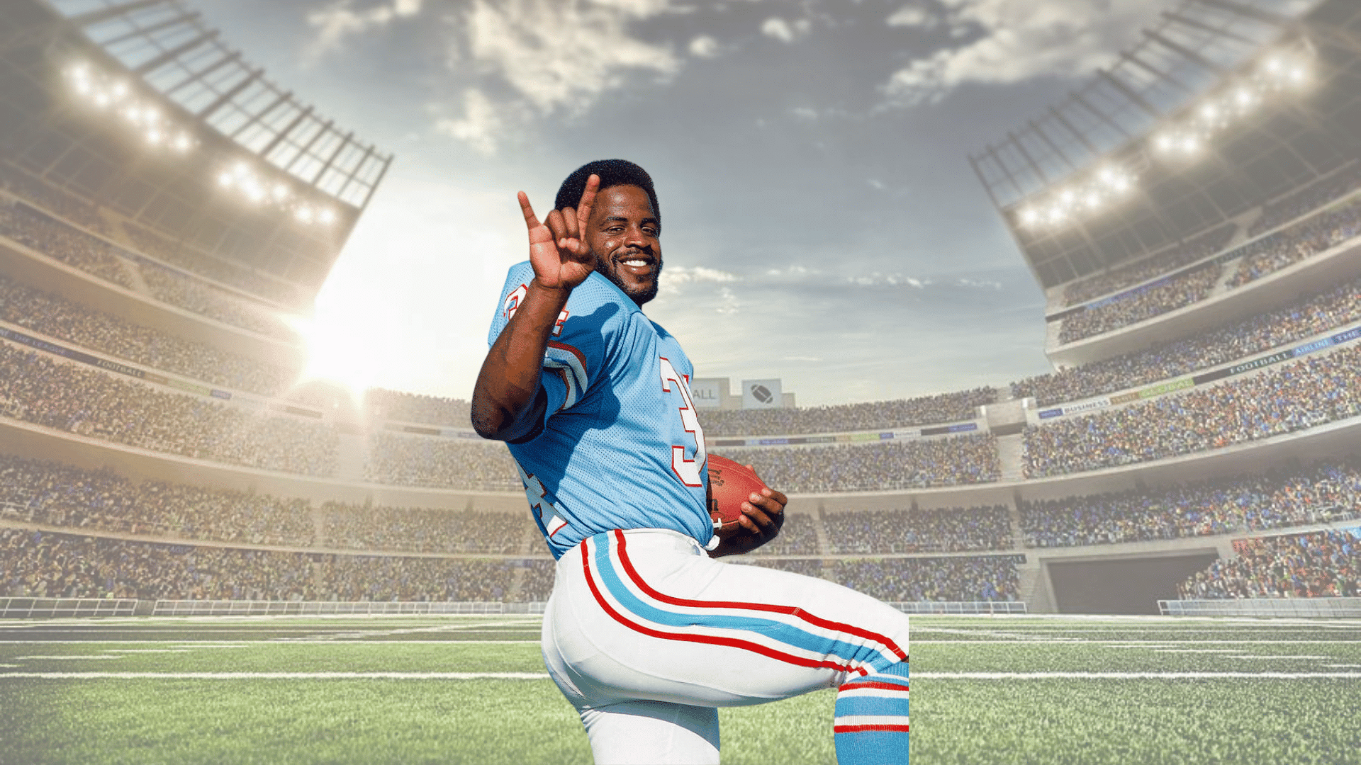 smiling football player in a blue uniform holding a football while raising one hand