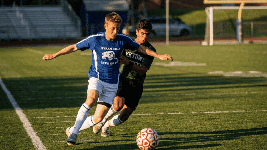 two soccer players competing for the ball while running closely together on a sunlit outdoor field during a match