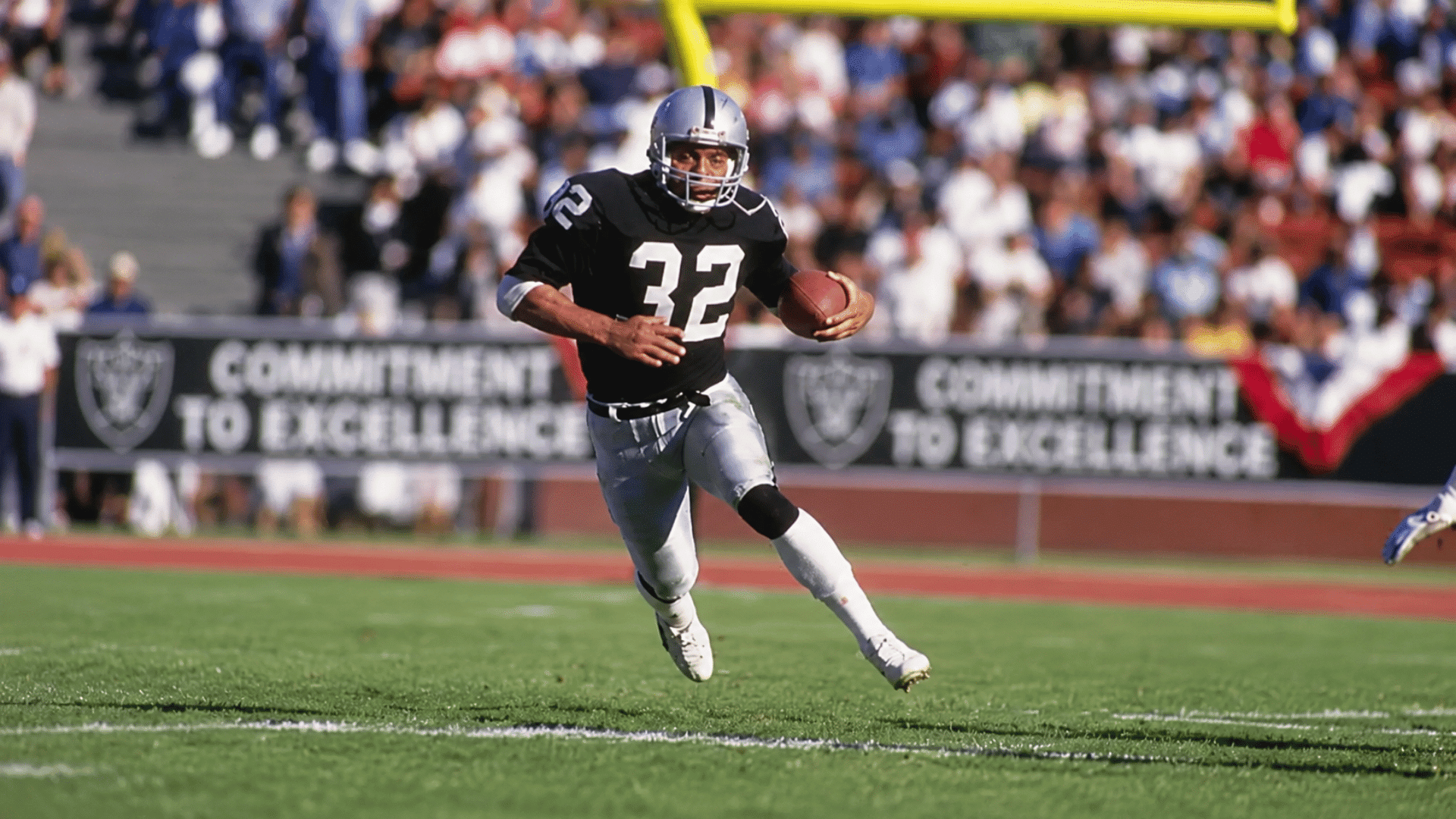 football running back wearing number 32 carrying the ball across the field during a game in a packed stadium
