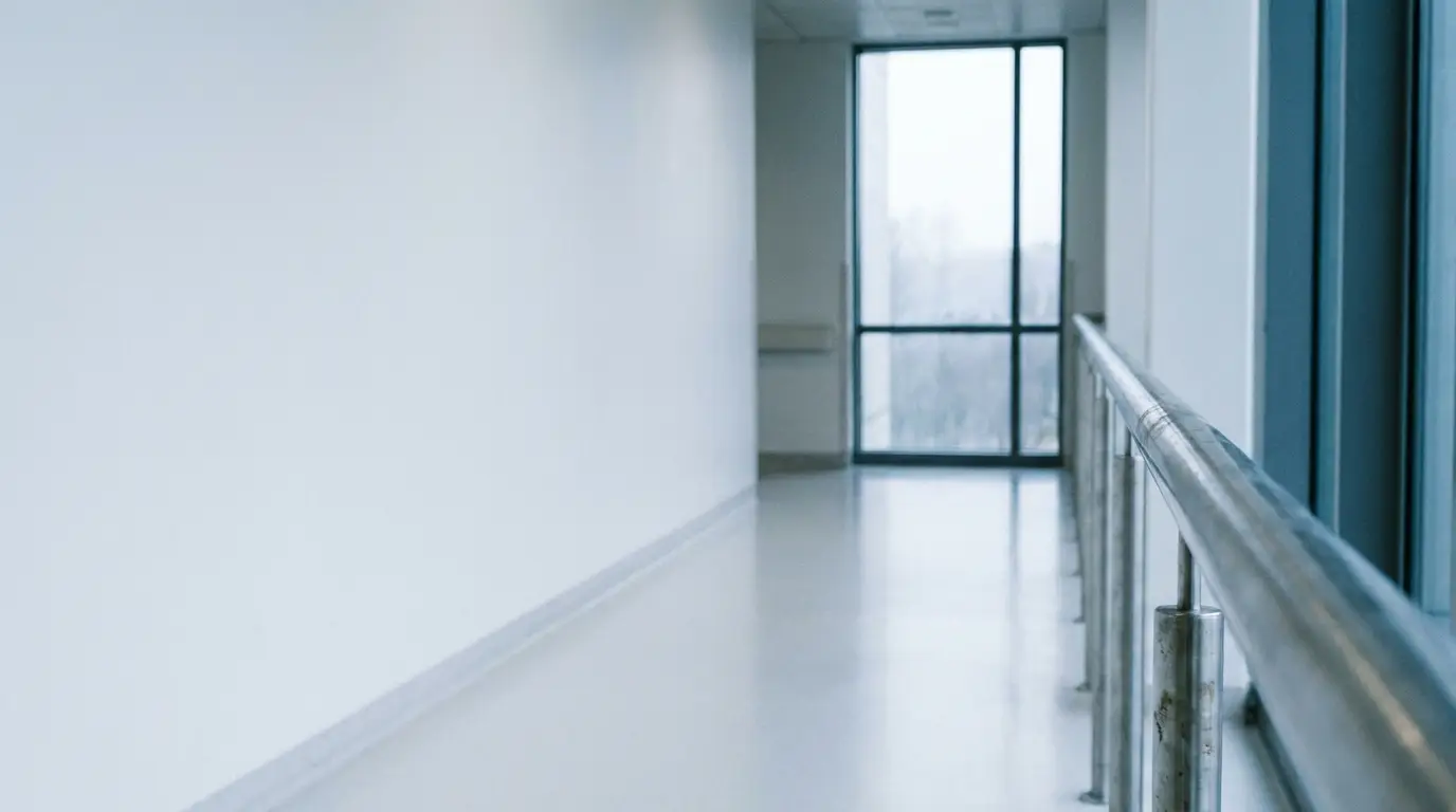 Empty hospital hallway with metal railing and large window in bright natural light