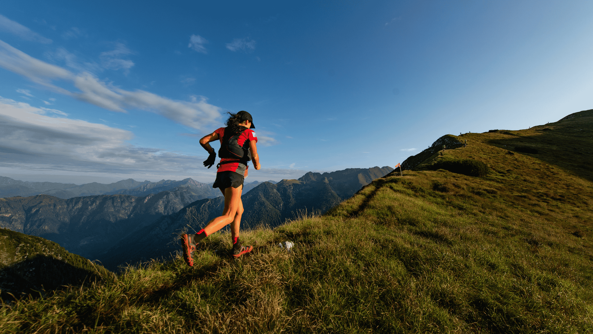 trail runner wearing a backpack running along a mountain ridge with scenic peaks in the distance