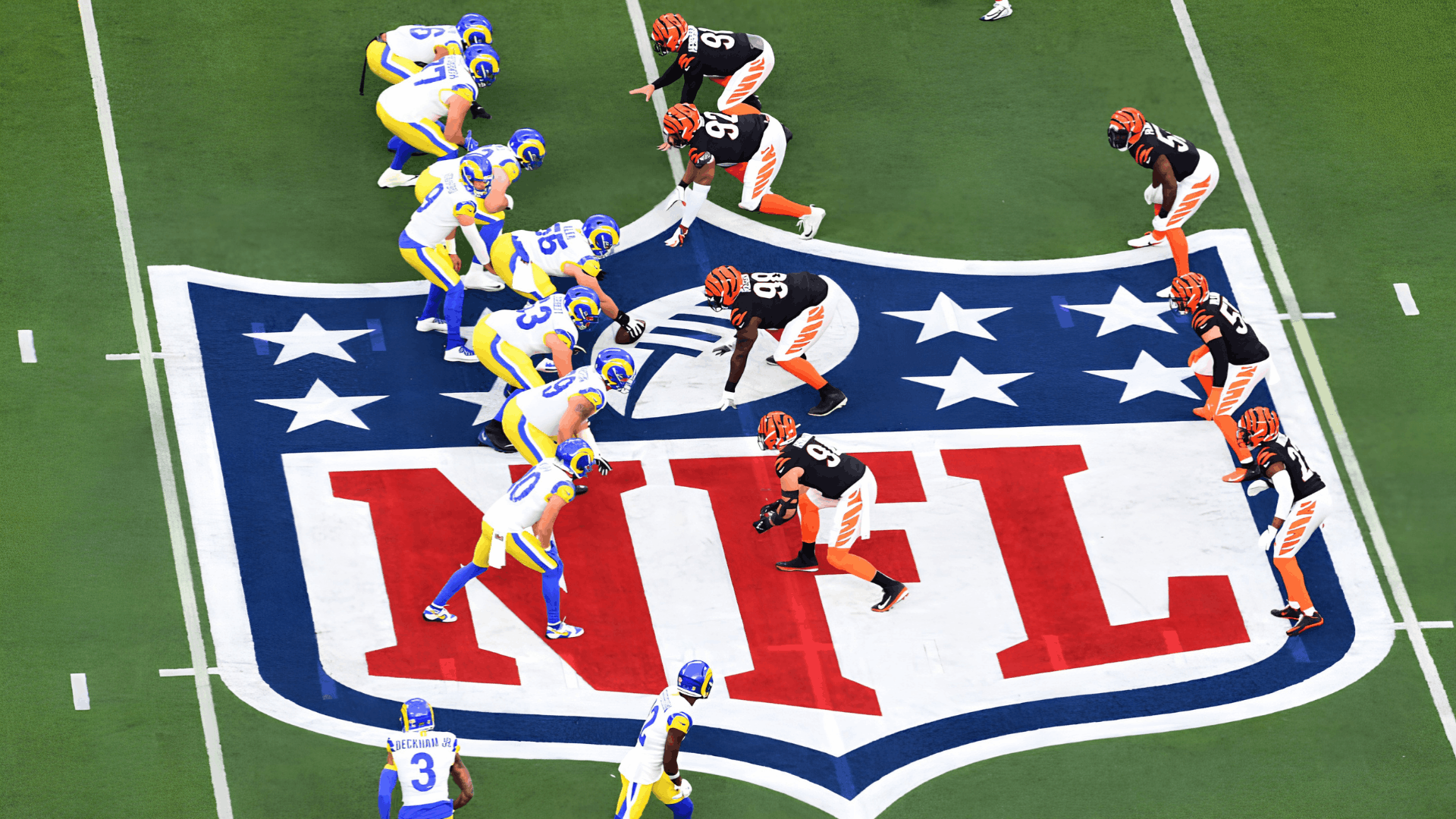 nfl players lined up at midfield on the league logo as the offense and defense prepare for the snap during a football game