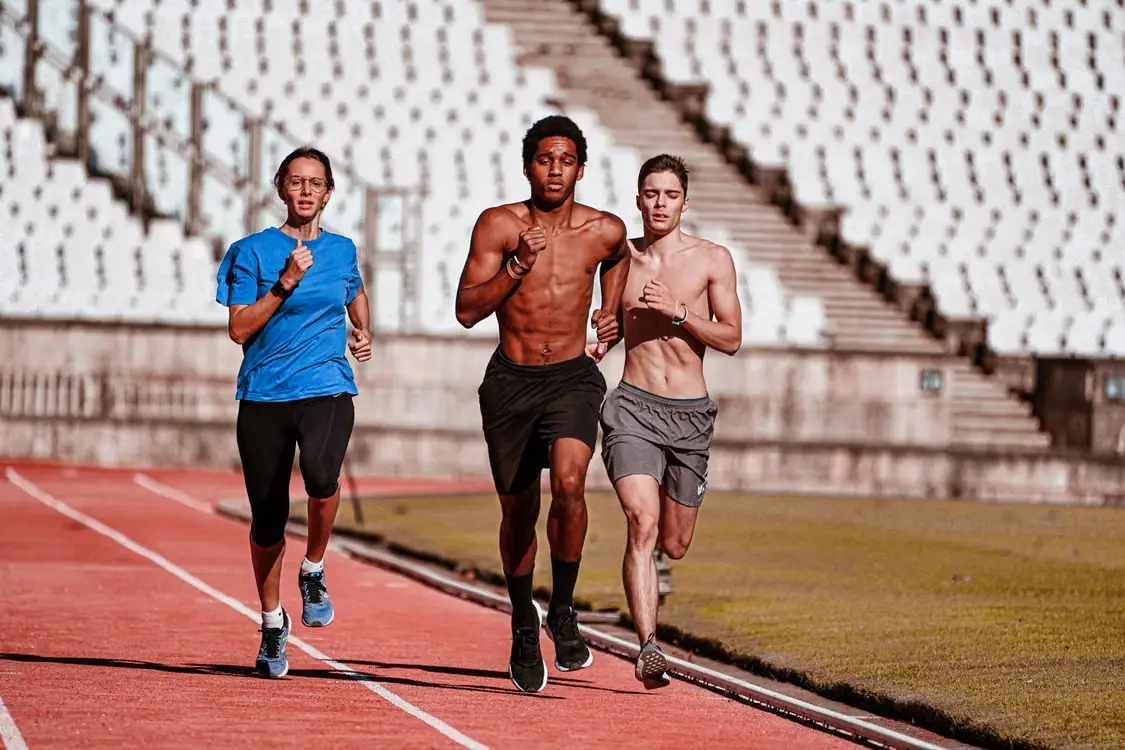 Three people jogging on a track in an outdoor stadium setting