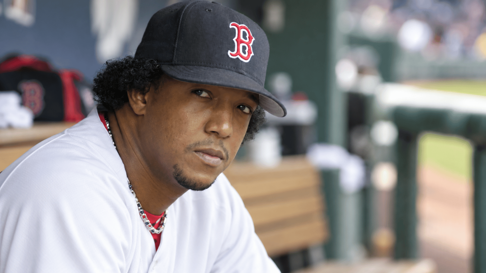 boston baseball pitcher wearing a dark team cap while sitting near the dugout during a game