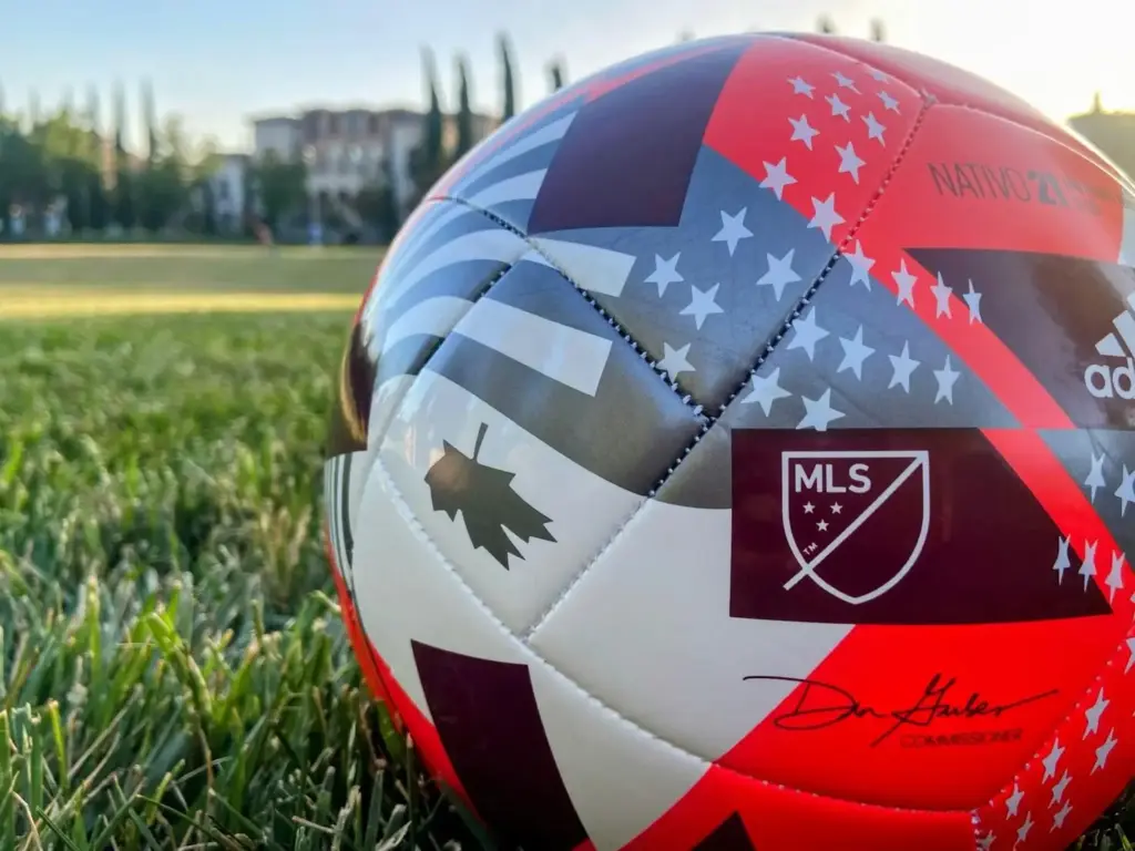 Soccer ball with MLS logo on grassy field during sunset