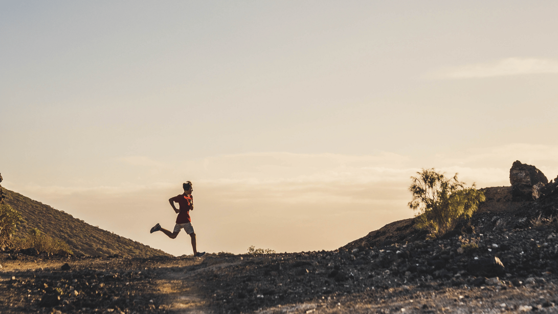 trail runner crossing a rocky mountain path during warm golden-hour light
