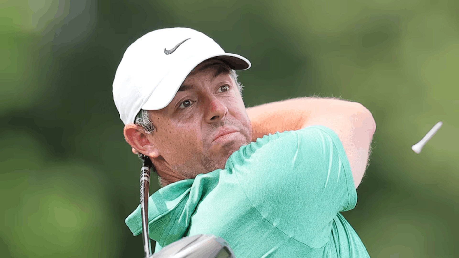 golfer in a white cap and green shirt following through after a powerful golf swing on the course