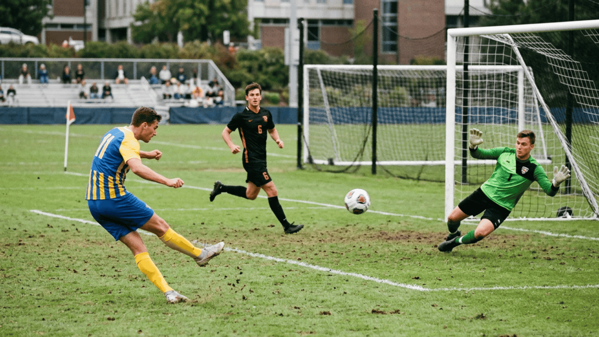 Soccer player taking a shot on goal as the goalkeeper dives to make a save during a match