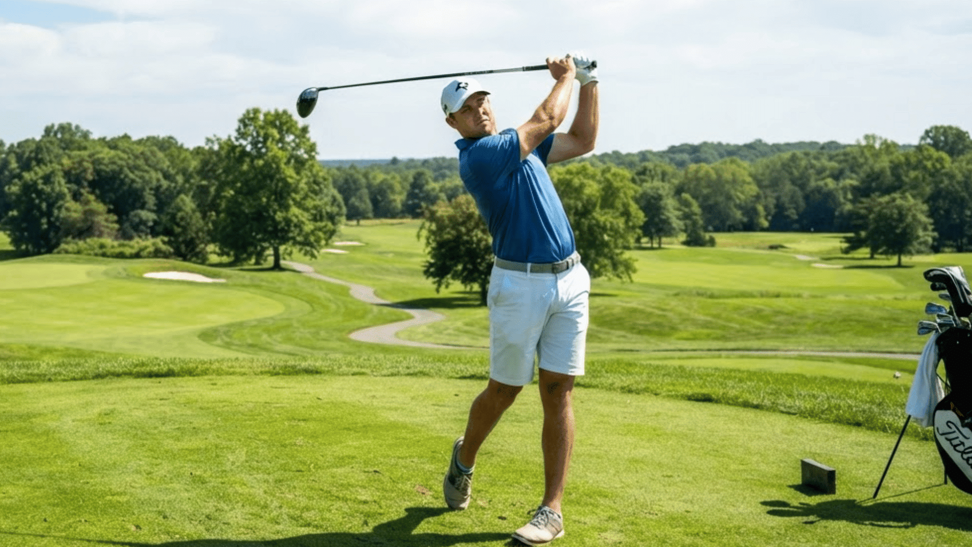 golfer completing a tee shot on a sunny golf course with fairways greens and bunkers in the background