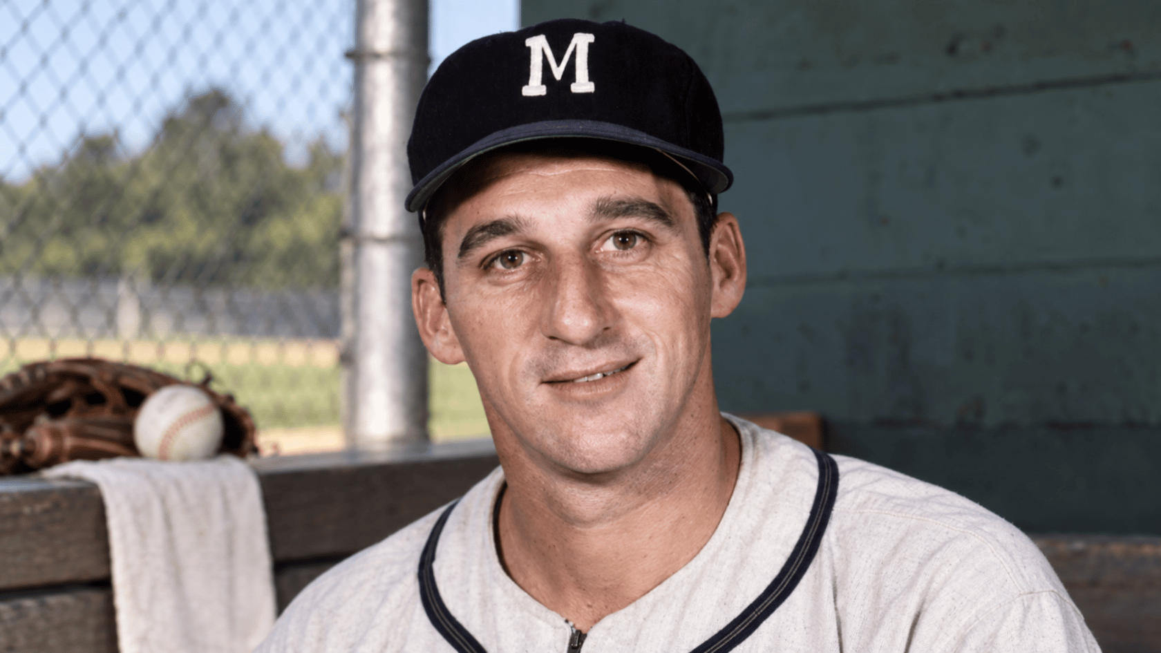 milwaukee baseball pitcher wearing a dark team cap while sitting inside the dugout with baseball equipment nearby