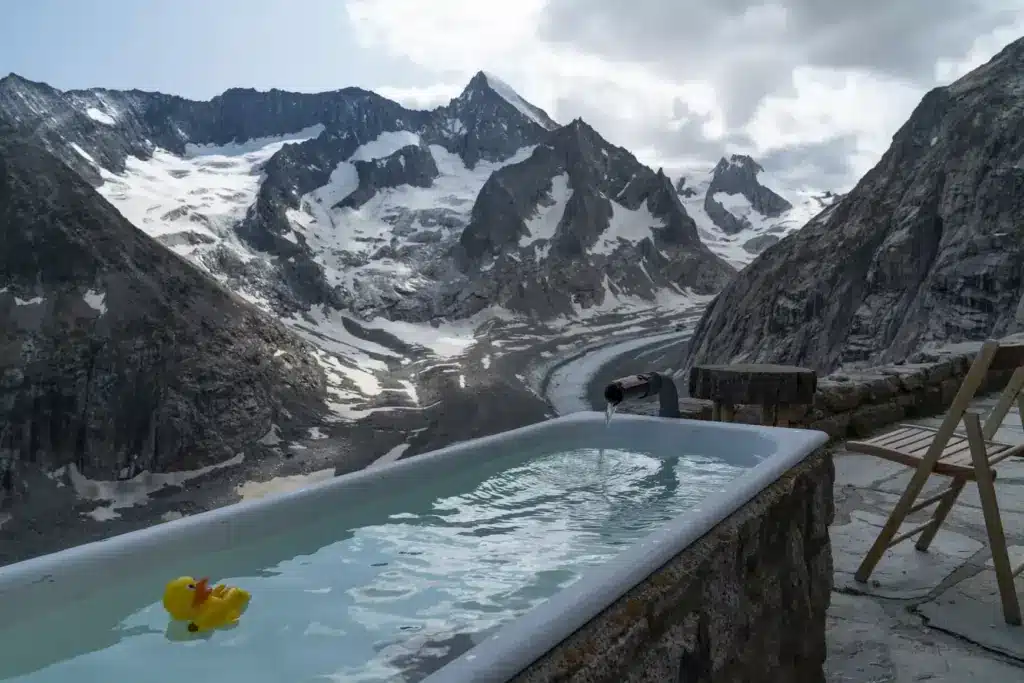 Outdoor bathtub with rubber duck overlooking snowy mountain landscape and cloudy sky