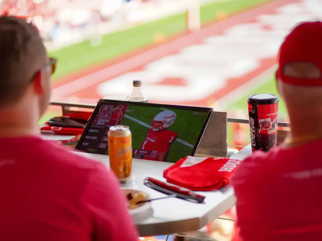 Fans watching football game on tablet at a stadium suite with drinks and snacks