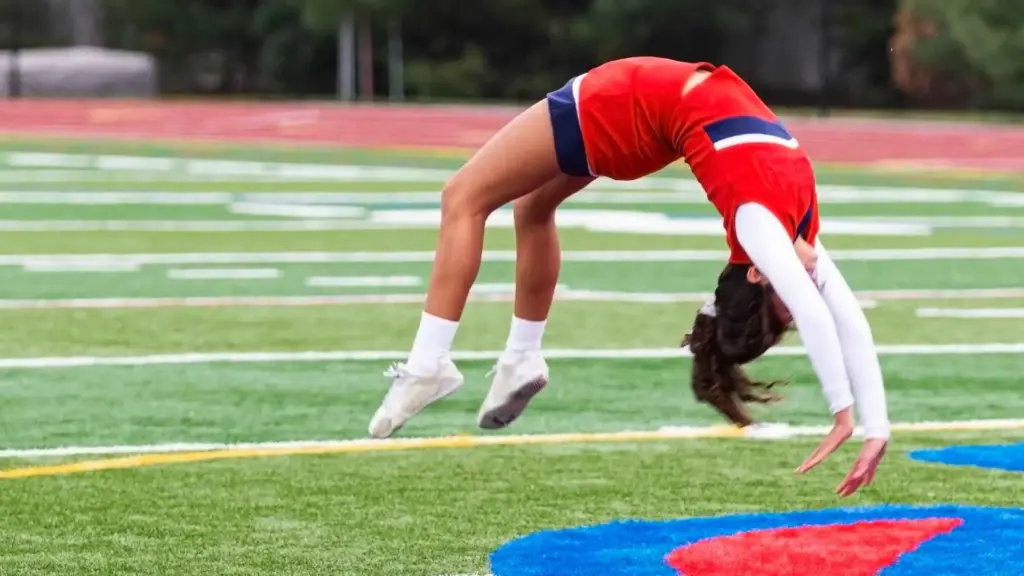 Cheerleader performing a backflip on a sports field in red and white uniform