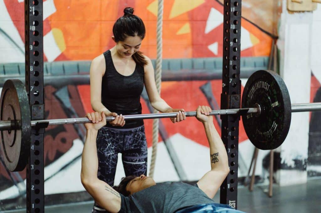 Person spotting another lifting barbell in colorful gym with graffiti walls