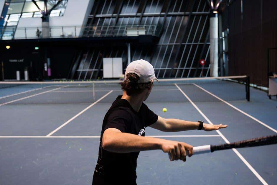 Tennis player preparing to hit ball on indoor court with modern architecture in background