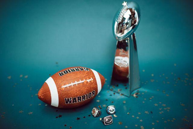 Football and championship rings beside silver trophy on blue background